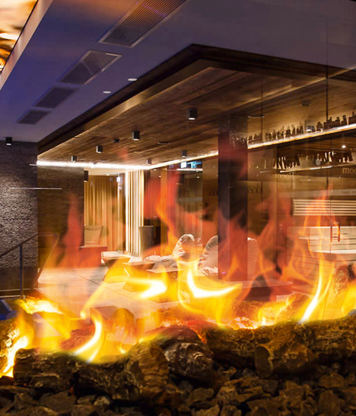 Elektrische Öfen für Hotels: Blick durch ein elektrisches Kaminfeuer in die Lounge Area eines Luxushotels